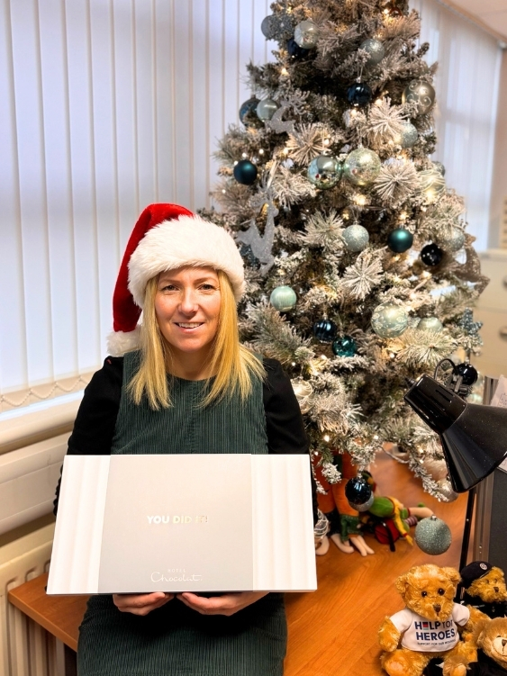 Joanne Foster wearing a Santa hat holding a box of chocolates next to the Demob Job Christmas tree, celebrating positive client feedback.